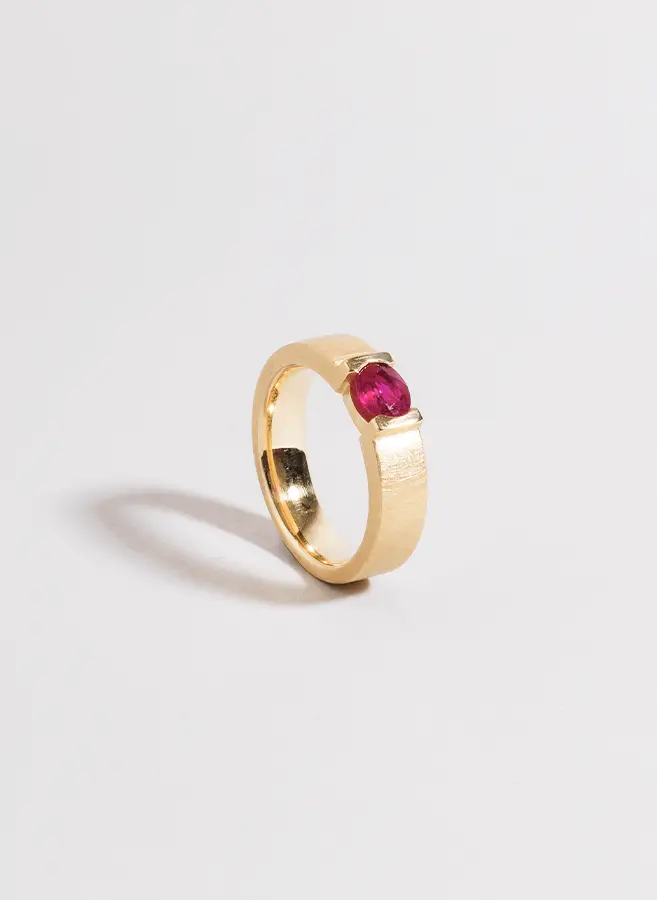 Zu sehen ist ein wunderschöner goldener Verlobungsring mit rotem Stein.